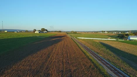 A-Drone-View-of-Crops-Waiting-to-be-Harvested-as-a-Stream-Passenger-Train-Approaches-During-the-Golden-Hour-on-a-Fall-Day