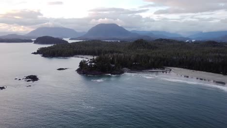 A-high-up-drone-video-of-a-forest-and-beach-area-with-mountains-and-clouds-in-the-background-during-sunset
