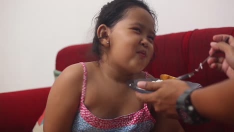 Aufgeregtes-Asiatisches-Kleines-Mädchen-Sitzt-Beim-Essen-Und-Wird-Von-Ihrem-Vater-Zu-Hause-Gefüttert