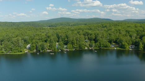 Aerial-drone-forward-moving-shot-over-lush-green-thick-vegetation-along-the-shore-of-sunset-lake-in-New-Hampshire,-USA-on-a-bright-sunny-day