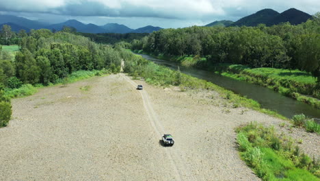 Aerial-Drone-Over-Four-Wheel-Drives-Off-Road-On-Gravel-Near-Creek-In-Australian-Countryside,-4K