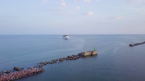 Aerial-view-of-large-white-cruise-liner-Seven-Seas-Splendor-arriving-at-the-port-of-Liepaja-,-early-morning-golden-hour,-water-transportation,-Baltic-sea,-vacation,-wide-shot-moving-forward