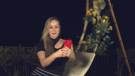 Latina-woman-taking-a-selfie-while-posing-on-a-swing-chair-outside-at-nighttime