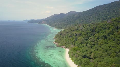 Aerial-view-of-lush-island-with-sandy-beach-and-clear-waters-in-Thailand---camera-tracking-and-pedestal-down