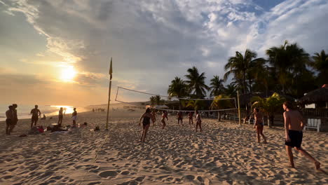 Beach-Volleyball-Match-on-Beautiful-Sandy-Shore-at-Sunset-in-Summer,-Puerto-Escondido-Mexico,-Group-of-Tourists-Playing-with-Ball-on-Seaside-Surrounded-by-Palms,-Tourism-Entertainment-and-Leisure
