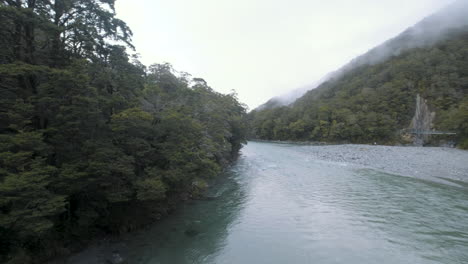 Panning-shot-of-blue-lake-surrounded-by-forrest,-mountains-and-mist-in-New-Zealand