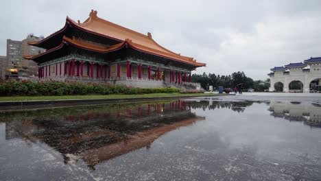 Puddle-reflection-from-Performing-Arts-Library-of-National-Theater-and-Concert-Hall-at-Liberty-Square-in-Taipei,-Taiwan---slow-tilt