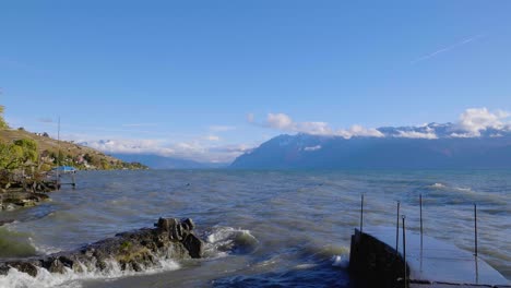 Waves-crashing-on-small-port-entrance-and-dismantled-railing-Shores-of-Lake-Léman,-the-Alps-in-the-background