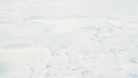 Slow-motion-shot-of-bird's-eye-view-from-airplane-over-ice-floes-in-ocean---tilt-up-to-clouds-and-blue-sky