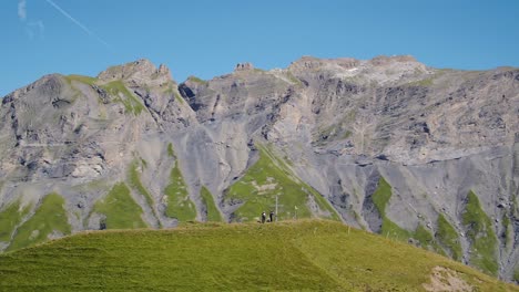 Orbiting-hikers-standing-on-hill-next-to-cross-with-high-mountains-in-the-background-Croix-de-Javerne---the-Alps,-Switzerland