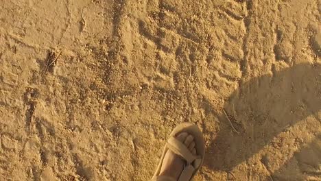 Ein-Mann-In-Sandalen-Geht-Einen-Unbefestigten-Weg-Mit-Reifenspuren-Im-Sand-Entlang