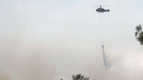 Footage-of-a-firefighting-helicopter-as-it-flies-over-a-forest-fire-and-dumps-its-water-bucket-on-the-fire-to-douse-the-flames