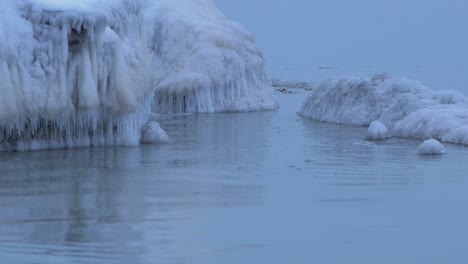 Kleine-Wellen,-Die-An-Einem-Bewölkten-Wintertag-Gegen-Die-Ruinen-Der-Nördlichen-Festung-Karosta-An-Der-Küste-Der-Ostsee-Brechen,-Bedeckt-Mit-Eis,-Schnee-Und-Eiszapfen,-Mittlere-Nahaufnahme