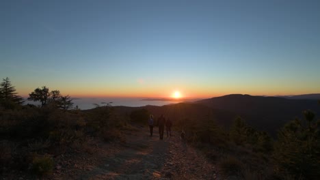 Three-people-and-a-dog-hiking-downhill-in-the-sunset