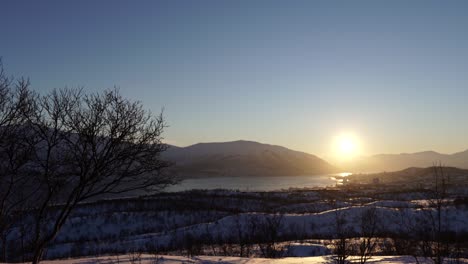 Video-of-a-snowy-winter-landscape-with-a-sunrise-sunset-over-the-city-of-Tromsø,-Norway