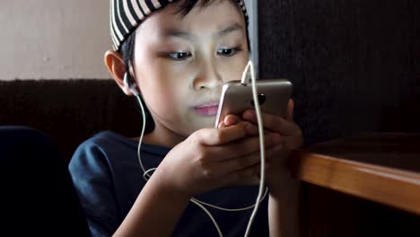 Junger-Südostasiatischer-Muslimischer-Junge,-Der-Sich-Videos-Auf-Dem-Handy-Ansieht,-Allein-Drinnen-In-Einem-Schwach-Beleuchteten-Raum
