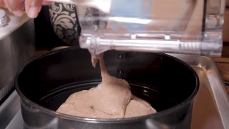 Pouring-brown-cake-batter-into-round-pan-in-kitchen,-Close-Up