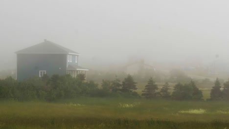 Nebel-Weht-über-Ein-Feld-Mit-Hohem-Gras-Mit-Einem-Einfachen-Blauen-Bauernhaus-Im-Hintergrund