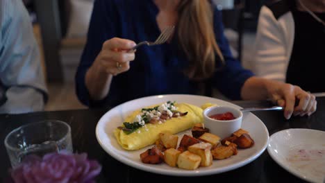 Woman-uses-knife-and-fork-to-cut-an-omelet-and-put-it-into-her-mouth
