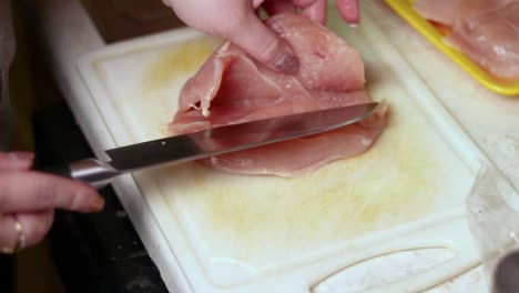 Carefully-cutting-a-piece-of-raw-chicken-breast-through-the-middle-in-length