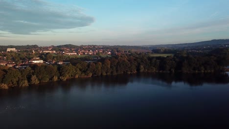 Forward-moving-aerial-drone-footage-over-lake-at-sunset-towards-countryside