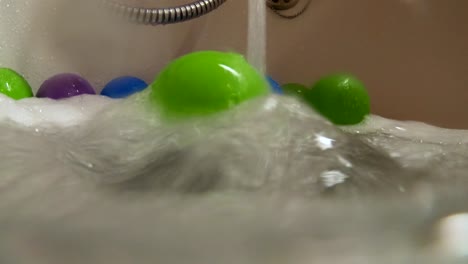 Green-plastic-ball-rolled-by-water-stream-in-bath-tub,-slow-motion,-colorful-home-scene,-relaxing-bubble-bath-for-children,-childhood-concept,-underwater-shot