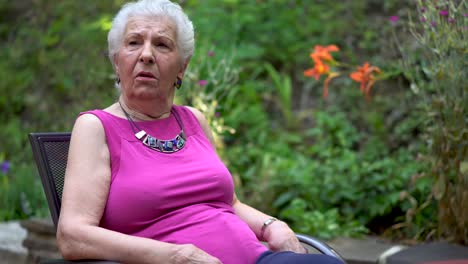 Elderly-woman-has-a-face-of-amazement-and-shock-while-sitting-outside-in-a-garden-area