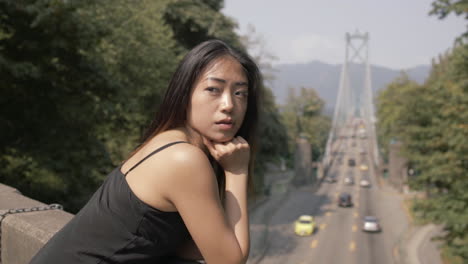 Medium-Closeup-of-Pretty-asian-woman-in-black-looking-behind,-Lions-gate-bridge-in-background,-Slowmo