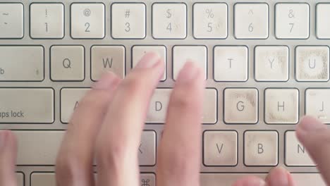 Medium-shot-of-hands-typing-on-a-worn-Mac-Keyboard