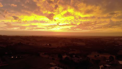 Forward-moving-aerial-shot-of-the-bright-orange-glow-of-the-sun-setting-on-the-horizon-in-rural-Australia