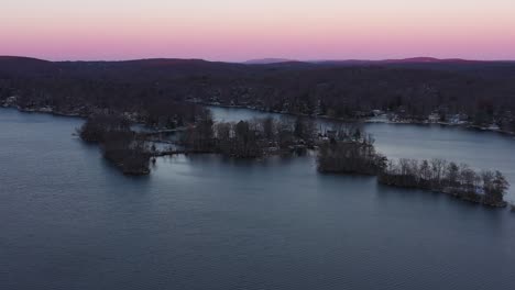 Drone-pullback-rise-over-winter-lake-in-forested-hills-at-sunset