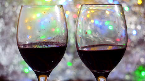 Two-wine-glasses-red-wine-sitting-on-moving-colorful-bokeh-and-silver-blanket-close-up-in-a-romantic-intimate-atmosphere