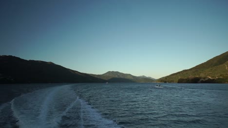 Early-morning-sunrise-boat-cruise-in-Marlborough-Sounds,-New-Zealand-with-small-boat-and-mountains-in-background