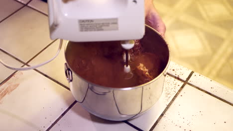 A-chef-in-a-kitchen-using-an-electric-mixer-to-make-chocolate-cake-batter-in-a-metal-mixing-bowl-with-the-powder-making-a-huge-mess
