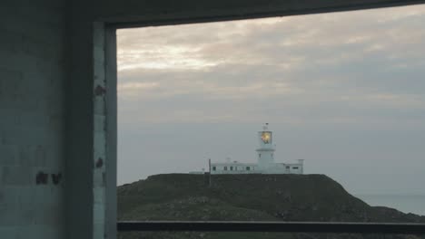 View-of-lighthouse-through-derelict-building-window-on-cloudy-evening