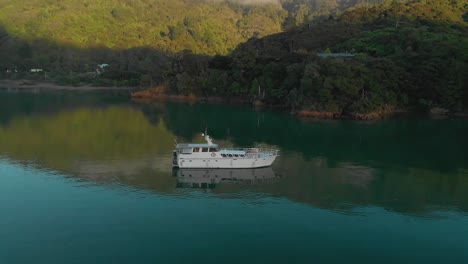 SLOWMO---Morning-aerial-flying-around-cruiser-boat-anchored-in-bay-in-Marlborough-Sounds,-New-Zealand