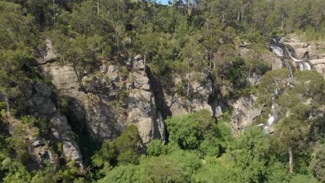 Forward-moving-aerial-shot-of-a-deep-canyon-leading-to-a-waterfall-in-the-bush-of-Australia