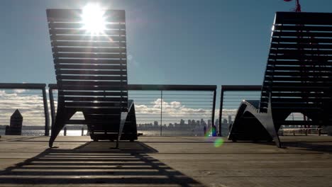 Sun-flares-streaming-through-deck-chairs-overlooking-harbor-and-cityscape