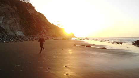 Menschen-Laufen-Bei-Sonnenaufgang-An-Einem-Malerischen-Sandstrand-Während-Eines-Fitnesstrainings-In-Santa-Barbara,-Kalifornien.-Luftdrohne