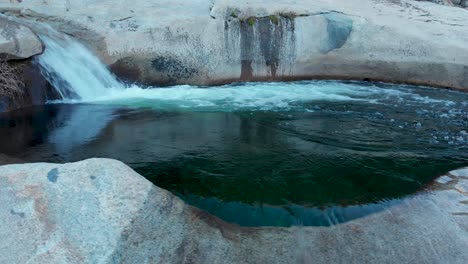 Panning-right-shot-of-waterfall-flowing-into-a-deep-pool-that-spill-out-over-slippery-granite-rock