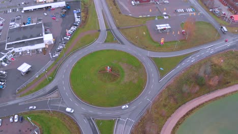 Drone-footage-moving-towards-a-roundabout-with-cars-driving-in-and-out-of-it,-on-a-cloudy-day-in-October