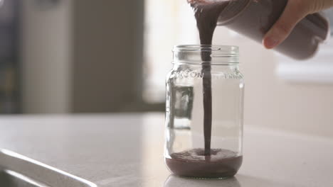 A-woman's-hand-pours-a-smoothie-into-a-reusable-glass-mason-jar-in-slow-motion