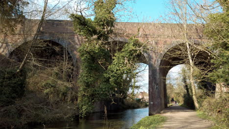Pan-along-high-arched-brick-railway-bridge-crossing-a-shallow-stream-in-the-countryside
