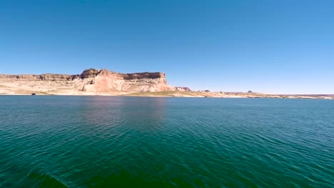 A-houseboat-cruises-through-the-turquoise-waters-of-Lake-Powell,-Page,-Arizona-passing-the-sandstone-buttes-that-ring-the-lake-shore