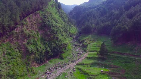 Dry-river-going-through-mountains,-Green-Hills-and-mountains-filled-with-trees-and-forest