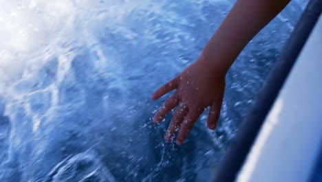 Zeitlupenaufnahme-Einer-Kinderhand,-Die-Das-Fließende-Wasser-Berührt,-Während-Ein-Kleines-Fischerboot-Auf-Dem-Atlantischen-Ozean-In-Portugal-Fährt