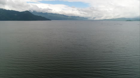 AERIAL:-Panoramic-shot-of-lake-sorrounded-by-mountains-and-blue-sky,-Yojoa,-Honduras
