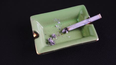 Fumar-Y-Dejar-Un-Cigarrillo-Enrollado-O-Un-Porro,-Marihuana-Legalizada-En-Un-Cenicero-Verde