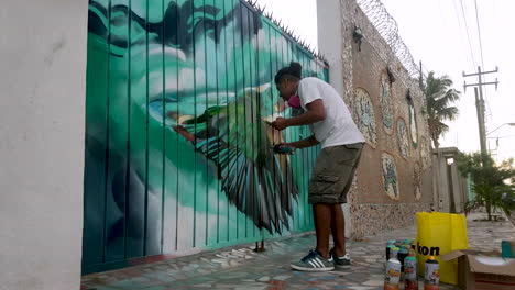 Graffiti-artist-is-spray-painting-a-tropical-bird-on-a-metal-gate