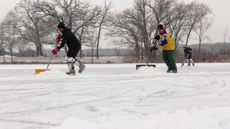 A-couple-adults-clean-the-snow-with-shovels-from-the-pond-hockey-field-facing-the-camera